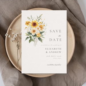 May include: A cream-colored wedding invitation with a watercolor floral design featuring yellow sunflowers and white daisies. The text reads "SAVE THE DATE" and includes the names Elizabeth & Andrew, the date May 26th, 2026, and "invitation to follow."