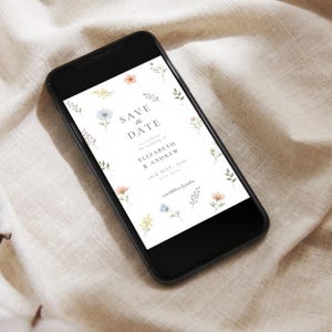 May include: A black smartphone displaying a digital Save the Date card with watercolor floral illustrations. The text reads: SAVE THE DATE to celebrate the wedding of ELIZABETH & ANDREW 26th MAY, 2036 City, State invitation to follow.