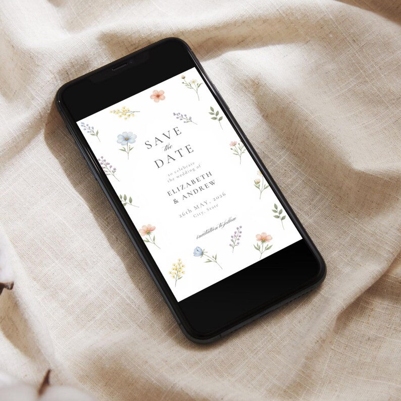 May include: A black smartphone displaying a digital Save the Date card with watercolor floral illustrations. The text reads: SAVE THE DATE to celebrate the wedding of ELIZABETH & ANDREW 26th MAY, 2036 City, State invitation to follow.