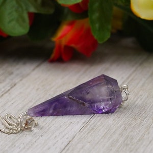 May include: A purple amethyst pendulum with a silver chain. The pendulum is a pointed crystal with a faceted design.