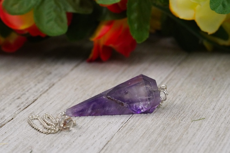 May include: A purple amethyst pendulum with a silver chain. The pendulum is a pointed crystal with a faceted design.