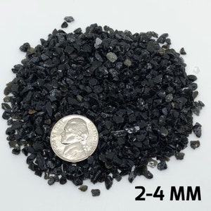 May include: A pile of black obsidian gravel, approximately 2-4 mm in size, with a US quarter for scale.