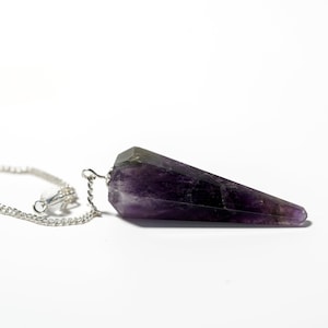 May include: A purple amethyst crystal pendulum with a silver chain. The crystal is faceted and has a pointed tip.