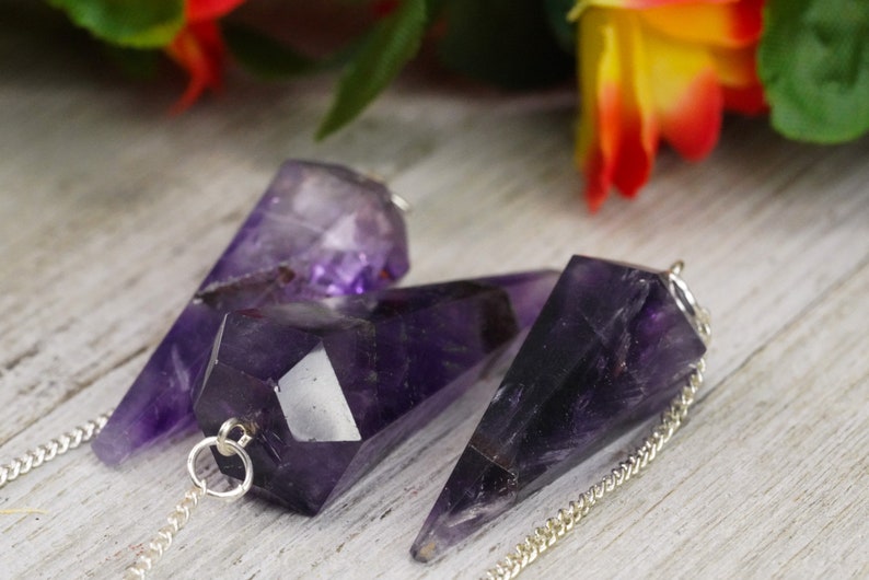 May include: Three amethyst crystal pendulums with silver chains. The crystals are faceted and have a deep purple color.