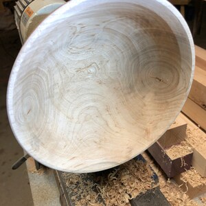 K&ouml;nnte beinhalten: Nahaufnahme einer Holzschale, die auf einer Drehbank gedreht wird. Die Schale ist aus hellem Holz mit einer sch&ouml;nen Maserung. Die Drehbank ist mit Holzsp&auml;nen bedeckt.