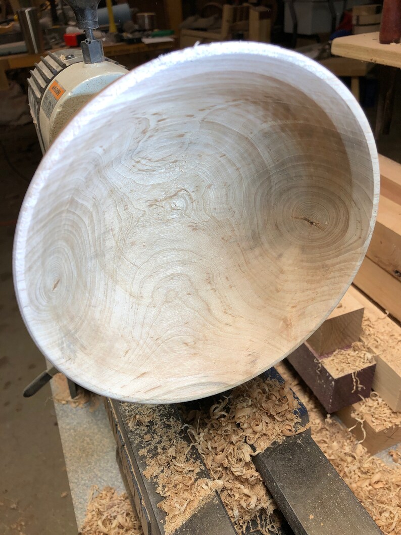 K&ouml;nnte beinhalten: Nahaufnahme einer Holzschale, die auf einer Drehbank gedreht wird. Die Schale ist aus hellem Holz mit einer sch&ouml;nen Maserung. Die Drehbank ist mit Holzsp&auml;nen bedeckt.