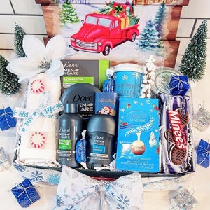 May include: A gift basket with a winter theme, featuring a red truck illustration. The basket contains Dove Men+Care products, a mug, chocolates, candies, and decorative elements like a bow and miniature trees.
