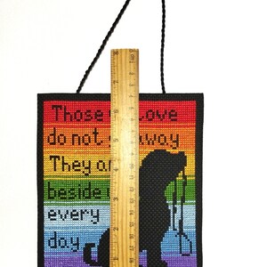 K&ouml;nnte beinhalten: Ein Regenbogenfarbener Kreuzstich-Wandbehang mit dem Text "Diejenigen, die es nicht wissen, sie sind jeden Tag an unserer Seite". Der Kreuzstich zeigt eine Silhouette einer Person, die eine Schaufel h&auml;lt.