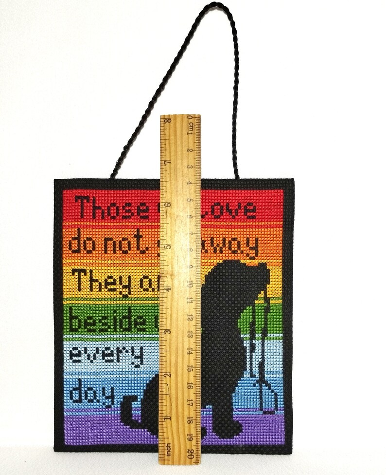 K&ouml;nnte beinhalten: Ein Regenbogenfarbener Kreuzstich-Wandbehang mit dem Text "Diejenigen, die es nicht wissen, sie sind jeden Tag an unserer Seite". Der Kreuzstich zeigt eine Silhouette einer Person, die eine Schaufel h&auml;lt.