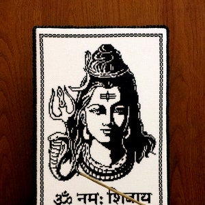 May include: Black and white cross-stitch embroidery of the Hindu deity Shiva. The image includes a depiction of Shiva's third eye, trishula, and a snake. The text "Om Namah Shivaya" is written below the image.