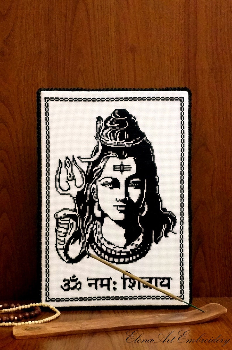 May include: Black and white cross-stitch embroidery of the Hindu deity Shiva. The image includes a depiction of Shiva's third eye, trishula, and a snake. The text "Om Namah Shivaya" is written below the image.