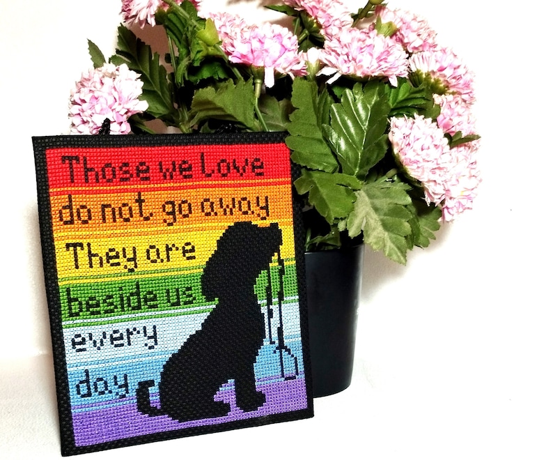 K&ouml;nnte beinhalten: Ein Regenbogenfarbener Kreuzstich mit einer schwarzen Silhouette eines Hundes. Der Kreuzstich lautet "Those we love do not go away. They are beside us every day."