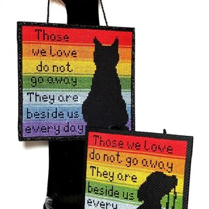 K&ouml;nnte beinhalten: Zwei Regenbogen-farbener Kreuzstich-Muster mit dem Text "Those we love do not go away. They are beside us every day." Ein Muster zeigt eine schwarze Katzensilhouette, das andere eine schwarze Hundesilhouette.