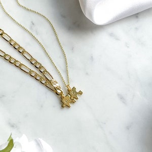May include: Two gold necklaces with a puzzle piece pendant. The necklaces are layered on a white marble surface.