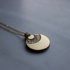 May include: A gold necklace with a round pendant featuring a textured design. The pendant has a smooth, shiny surface and a smaller, textured circle in the center.