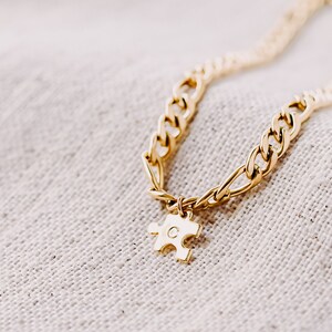 May include: A gold chain necklace with a gold puzzle piece charm. The puzzle piece has the letter "C" engraved on it.