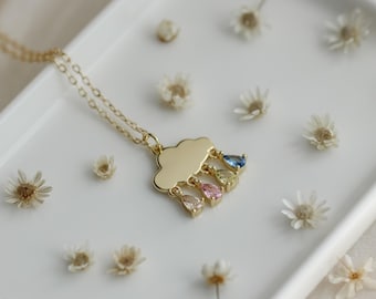 May include: A gold necklace with a cloud pendant and four teardrop-shaped gemstones in blue, yellow, pink, and light pink.