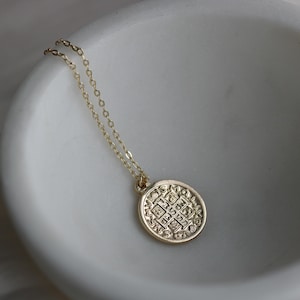 May include: A gold chain necklace with a round pendant featuring an intricate design and inscription. The pendant is a circular coin with a raised design and text.