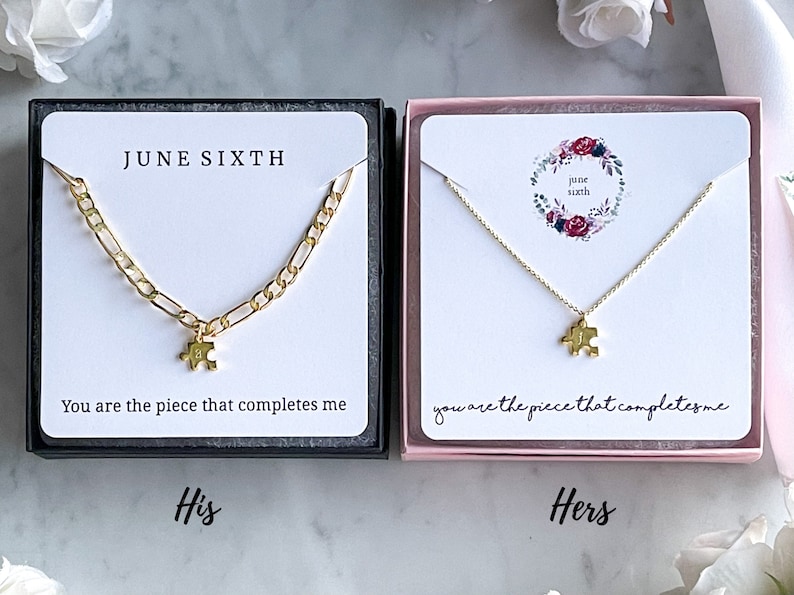May include: Two gold necklaces with puzzle piece pendants in black and pink boxes. The necklaces are accompanied by cards that read "You are the piece that completes me." and "JUNE SIXTH".