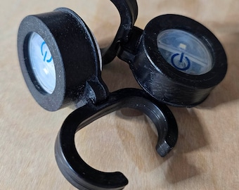 Könnte beinhalten: Zwei schwarze Fahrradlichter mit einem Haken zum Anbringen an einem Fahrrad. Jedes Licht hat eine klare Linse mit einem blauen Ein-/Ausschalter.