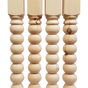 May include: Four unfinished wooden table legs. Each leg features a square top, a series of rounded spheres, and a tapered base. The wood grain is visible, and the legs are ready for staining or painting.