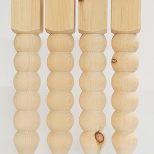 Peut inclure: Quatre pieds de table en bois non finis avec un design arrondi et perlé. Les pieds sont en bois naturel et ont une couleur brun clair.