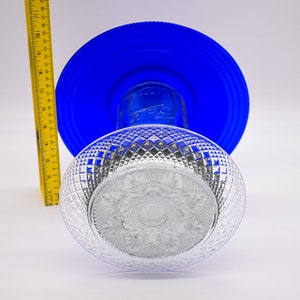 May include: A clear glass bowl with a diamond pattern sits on top of a blue glass plate. The bowl has a decorative design in the center.