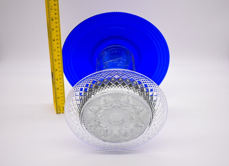 May include: A clear glass bowl with a diamond pattern sits on top of a blue glass plate. The bowl has a decorative design in the center.
