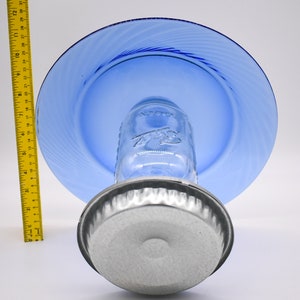 May include: A blue glass plate sits atop a clear glass jar with a silver lid. The jar is sitting on a silver metal base.