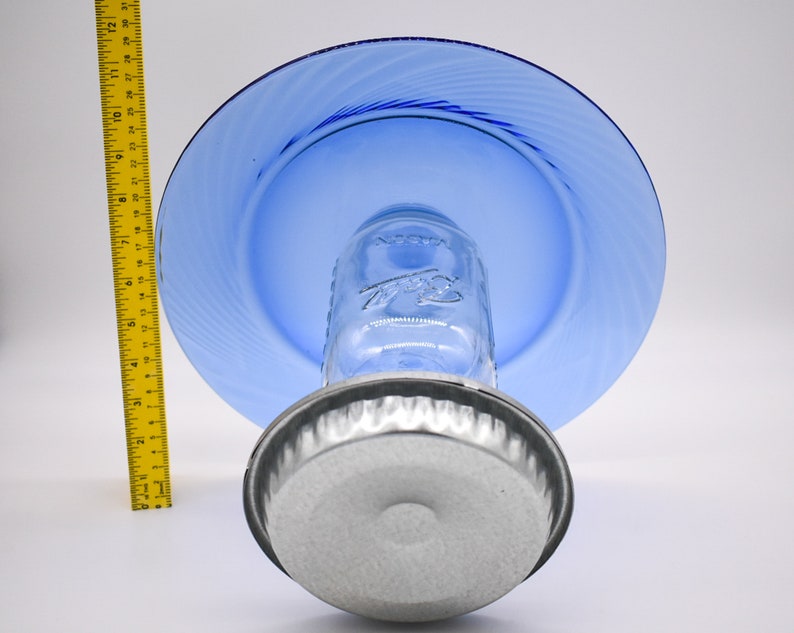 May include: A blue glass plate sits atop a clear glass jar with a silver lid. The jar is sitting on a silver metal base.