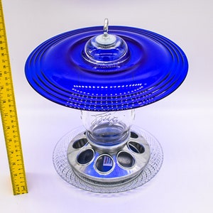 May include: A blue glass bird feeder with a metal base and a clear glass jar. The feeder has a unique design with a layered blue glass top.