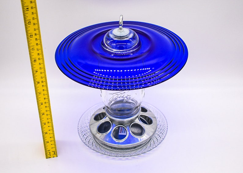 May include: A blue glass bird feeder with a metal base and a clear glass jar. The feeder has a unique design with a layered blue glass top.