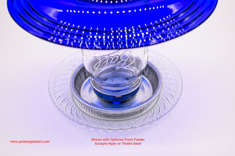 May include: Blue glass bird feeder with a clear glass jar and a metal base. The feeder is shown with an optional finch feeder.  Shown with Optional Finch Feeder Excepts Nyjer or Thistle Seed