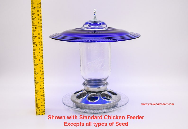 May include: A blue glass bird feeder with a clear glass jar and a metal base. The feeder is shown with a standard chicken feeder.  Shown with Standard Chicken Feeder Excepts all types of Seed www.yankeeglassart.com