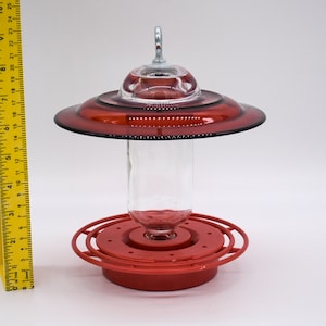 Red glass hummingbird feeder with a clear glass bottle and a red plastic base. The feeder has a red glass saucer with a clear glass dome on top.