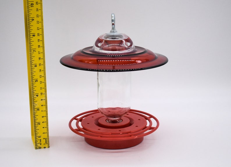 Red glass hummingbird feeder with a clear glass bottle and a red plastic base. The feeder has a red glass saucer with a clear glass dome on top.