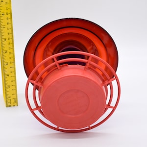 Red hummingbird feeder with a red base and a black and red top. The feeder has a wire cage around the base and the words 'Hummingbird Feeder' are printed on the base.