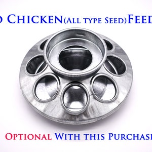 May include: A silver metal chicken feeder with a round base and multiple circular openings for seed. The feeder has a central ring for holding seed. The text "STD CHICKEN (ALL TYPE SEED) FEEDER" is printed in blue on a white background.
