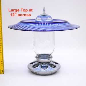 May include: A blue glass bird feeder with a 12-inch diameter top, a clear glass jar for holding birdseed, and a metal base with feeding ports.