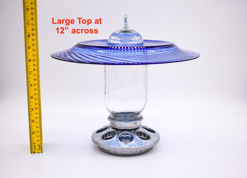 May include: A blue glass bird feeder with a 12-inch diameter top, a clear glass jar for holding birdseed, and a metal base with feeding ports.