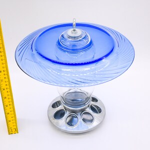 May include: A blue glass bird feeder with a clear glass reservoir and a silver metal base with multiple feeding ports.