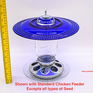 May include: A blue glass bird feeder with a metal base and a clear glass jar. The feeder is shown with a standard chicken feeder.  Excepts all types of seed. www.yankeeglassart.com