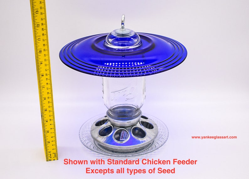 May include: A blue glass bird feeder with a metal base and a clear glass jar. The feeder is shown with a standard chicken feeder.  Excepts all types of seed. www.yankeeglassart.com