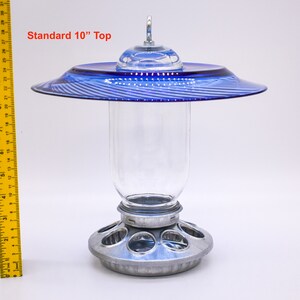 May include: A blue glass bird feeder with a 10-inch top and a clear glass jar. The feeder has a metal base with multiple feeding ports.