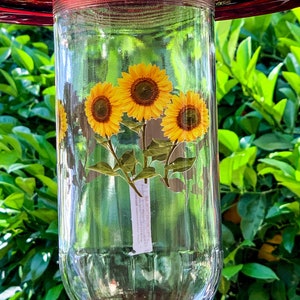 May include: A clear glass hummingbird feeder with a red top and a sticker of three yellow sunflowers on the front.
