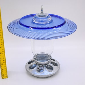 May include: A blue glass bird feeder with a clear glass jar and a metal base with multiple feeding holes.