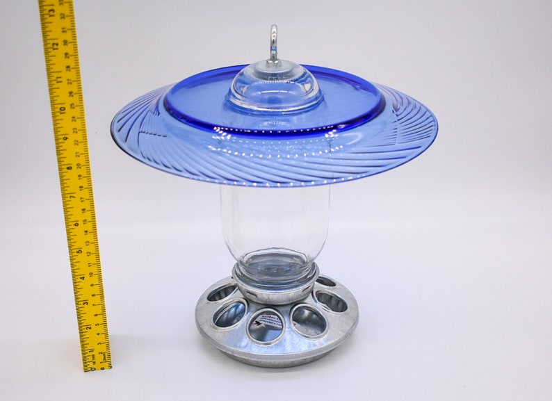 May include: A blue glass bird feeder with a clear glass jar and a metal base with multiple feeding holes.