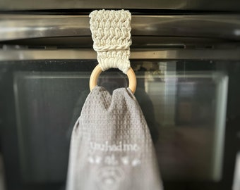 Puede incluir: Un anillo de toalla de crochet blanco con un anillo de madera colgado de una puerta de horno de plata. La toalla es gris con el texto "You had me at..." bordado.