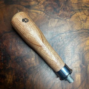 May include: A wooden coffee tamper handle with a paw print design and a silver metal base. The handle is made of light brown wood and has a smooth finish.