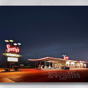 Pode incluir: Uma vista noturna de um restaurante retro chamado "Scotty's Hamburgers" com letreiros de néon vermelhos. O restaurante tem um telhado plano com um dossel e um grande estacionamento. Um carro preto está estacionado em frente ao restaurante.